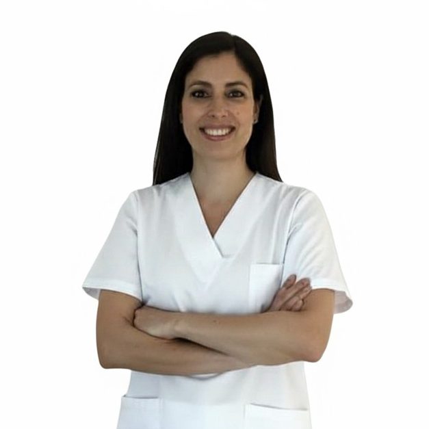 Fisioterapeuta a domicilio con bata blanca sonriente, brazos cruzados y fondo blanco.