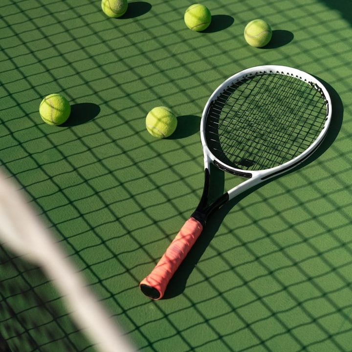 Raqueta de tenis con varias pelotas verdes sobre una cancha de tenis.