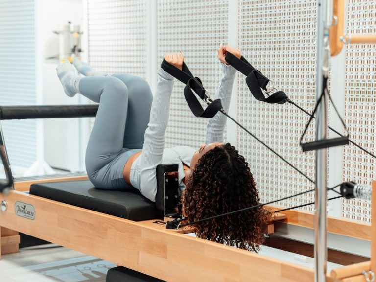 Mujer haciendo ejercicio en un reformador de pilates, en posición de piernas elevadas.