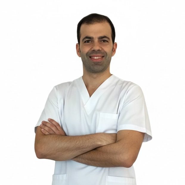 Fisioterapeuta a domicilio sonriente con bata blanca, brazos cruzados y fondo blanco.