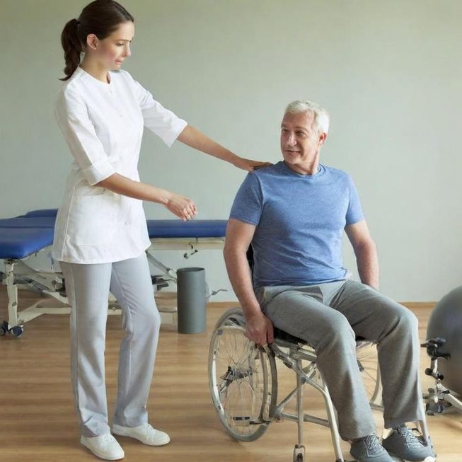 Una fisioterapeuta ayuda a un hombre mayor en silla de ruedas en un entorno clínico.