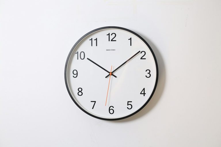 Reloj de pared redondo con fondo blanco y manecillas negras y naranja.